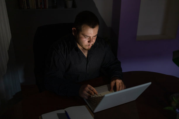 一个年轻人晚上在笔记本电脑前完成他的工作。图片下载