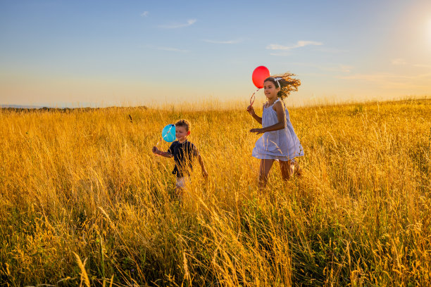 兄弟姐妹们一边玩气球，一边迎着天空在草地上奔跑图片下载
