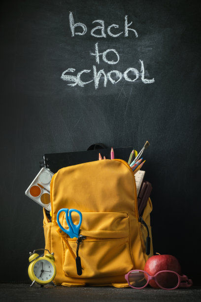 黄色背包与学校用品旁边的地球仪，红色的苹果和眼镜在黑色的学校董事会背景。九月一日回到学校概念图片下载