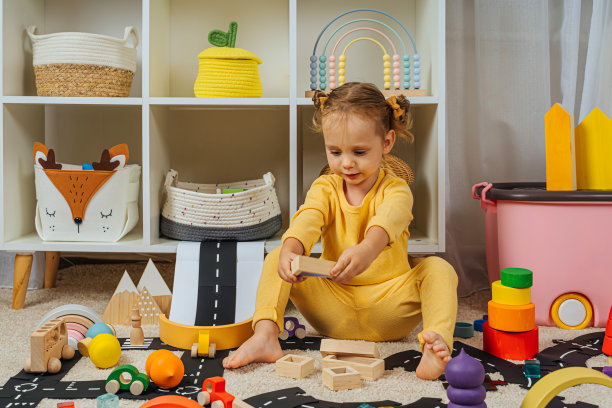 一个小女孩坐在地板上玩玩具，木块，汽车和道路在游戏室。现代幼儿园幼儿教育游戏。图片下载