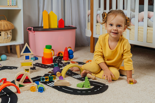 一个小女孩坐在地板上玩玩具，木块，汽车和道路在游戏室。现代幼儿园幼儿教育游戏。图片下载