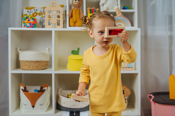 蹒跚学步的孩子在看彩色的玩具窗户。现代幼儿园幼儿教育游戏。一个小女孩在看透明的彩色积木玩具。木制彩虹堆叠块。图片下载