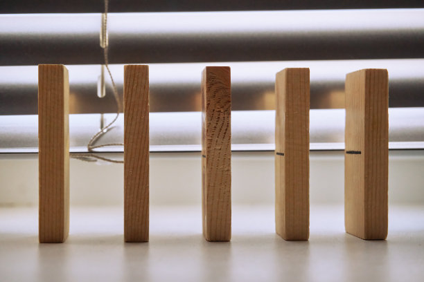 木制的多米诺骨牌彼此垂直地站在一起，背景是垂直的百叶窗。有选择性的选择聚焦图片下载