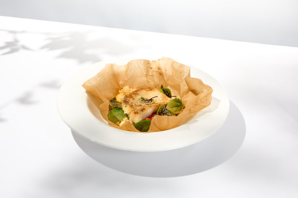 烤鳕鱼片配羊皮纸蔬菜。烤鳕鱼排配菜花。夏季菜单上的健康食品。羊皮纸烤的白鱼。鱼盘在白色的背景与阴影。图片下载