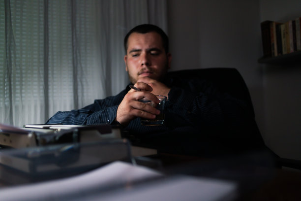 年轻的作家坐在家里的办公室里喝着酒想着该在他的旧打字机上写些什么想着该讲什么故事。图片下载
