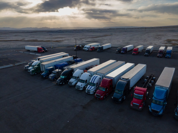 在犹他州东部沙漠地区70号州际公路上的一个大型停车场，半挂卡车排队等待晚上在一个戏剧性的云景日落天空下图片下载