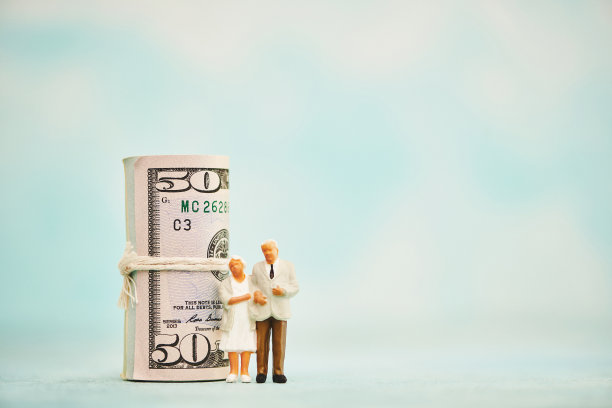 一对年长的夫妇站在一卷美元旁边。退休及退休金主题图片下载