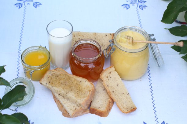 桌上摆着静物，白色桌布上有蓝色刺绣——几罐蜂蜜、自制面包和一杯牛奶图片下载