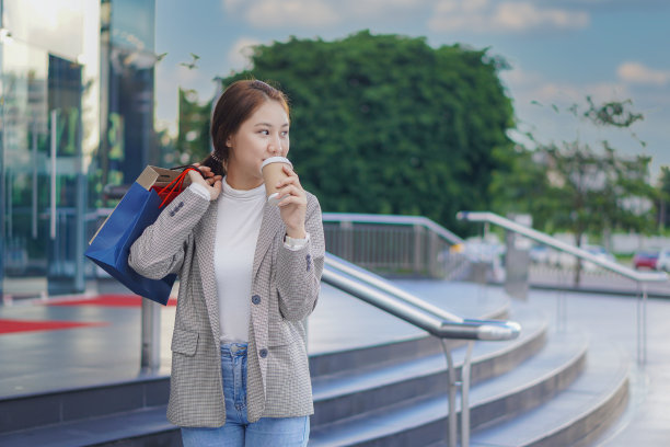 在购物中心前，一位拿着五颜六色的购物袋的亚洲女性正对着自己的名字微笑。图片下载