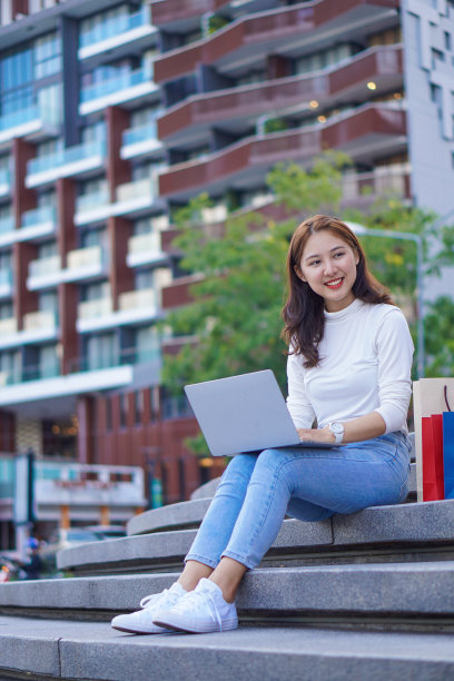拿着五颜六色的购物袋的亚洲女性坐在百货商店前，用笔记本电脑愉快地网购。图片下载