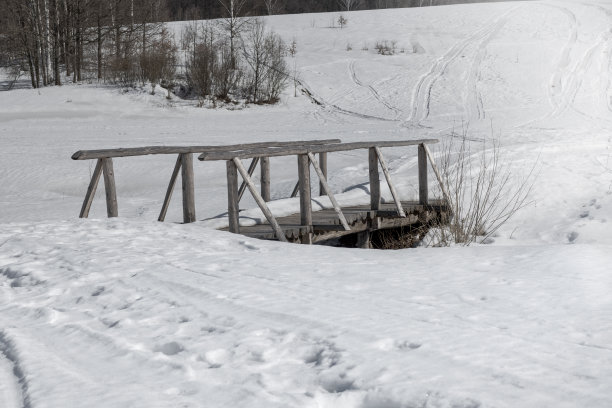 冬季景观与木桥在冻结的小溪和雪与小径在农村丘陵地区。图片下载