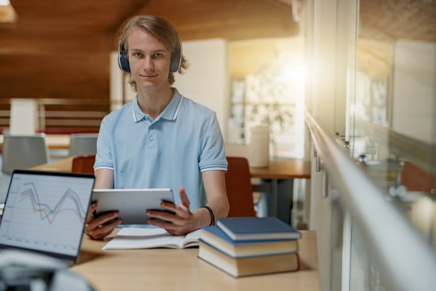 男学生戴着耳机坐在图书馆，用数字平板电脑学习图片下载
