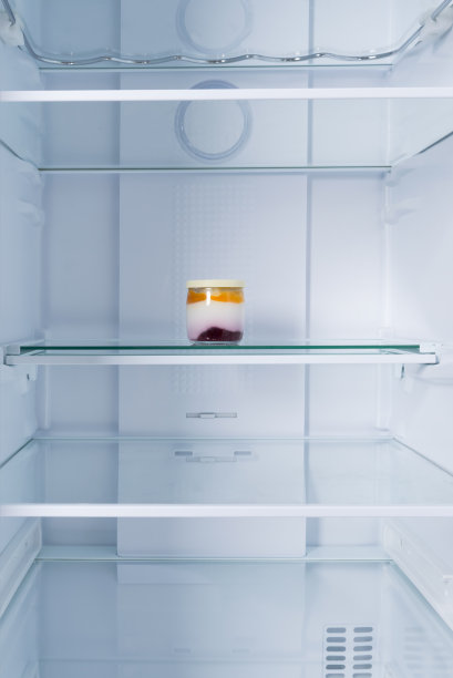 在白色冰箱的背景下，架子上有一个装着牛奶酸奶和果酱的玻璃罐图片下载