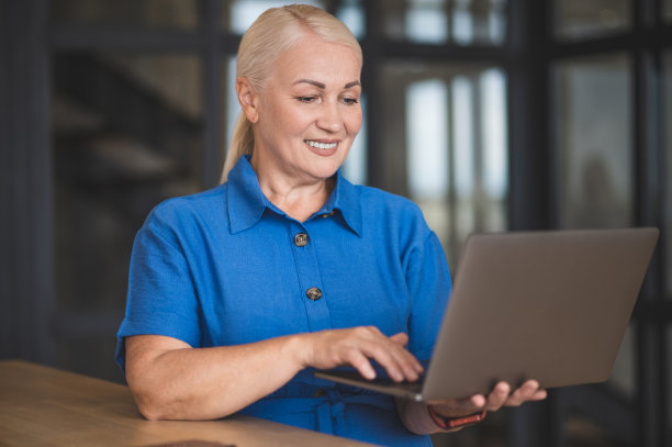 一个穿着蓝色裙子的女人微笑着在笔记本电脑上工作图片下载