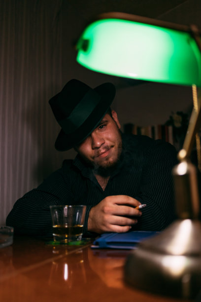 一个戴着帽子的男人的肖像，抽着雪茄，在他的办公桌上喝着饮料。图片下载