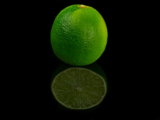 整个青柠放在黑色的背景上，还有切过的青柠的倒影图片下载