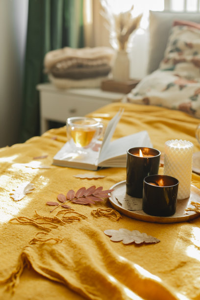 室内舒适的斯堪的纳维亚秋色卧室。燃烧的蜡烛，一杯茶，打开的书在床上。垂直的图像图片下载