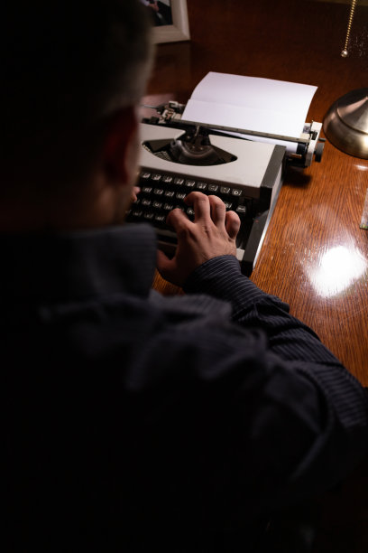 年轻的作家坐在他家里的房间里，用他的旧打字机写故事，思考故事应该写在哪里，然后检查他的文本，写。图片下载
