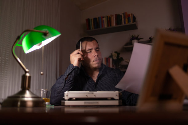 年轻的作家坐在他家里的房间里，用他的旧打字机写故事，思考故事应该写在哪里，然后检查他的文本，写。图片下载