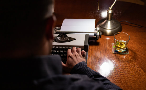 年轻的作家坐在他家里的房间里，用他的旧打字机写故事，思考故事应该写在哪里，然后检查他的文本，写。图片下载