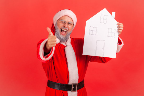 身穿圣诞老人服装、手拿纸房子的灰胡子老人兴奋地竖起大拇指，推荐房地产中介。图片下载