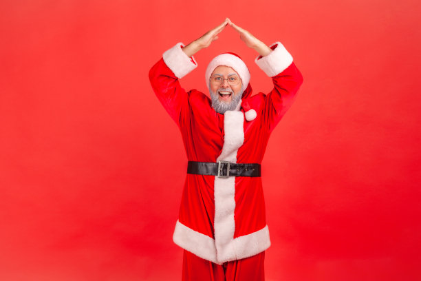 穿着圣诞老人服装的灰胡子老人兴奋地举起双手，做着屋顶的手势，梦想着房子作为圣诞礼物。图片下载