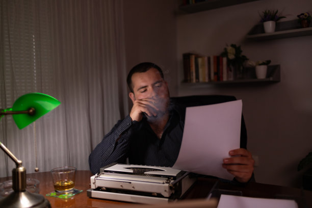 年轻的作家坐在他家里的房间里，用他的旧打字机写故事，思考故事应该写在哪里，然后检查他的文本，写。图片下载