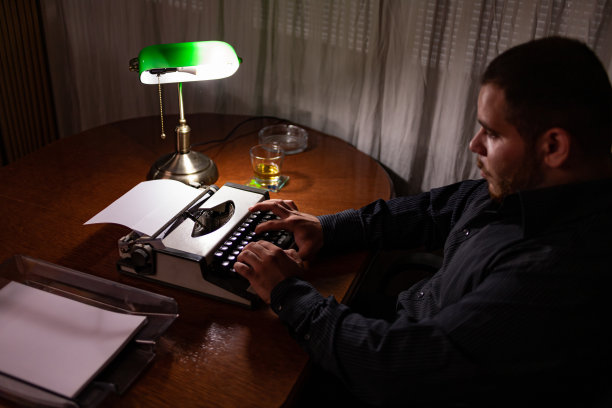 年轻的作家坐在他家里的房间里，用他的旧打字机写故事，思考故事应该写在哪里，然后检查他的文本，写。图片下载