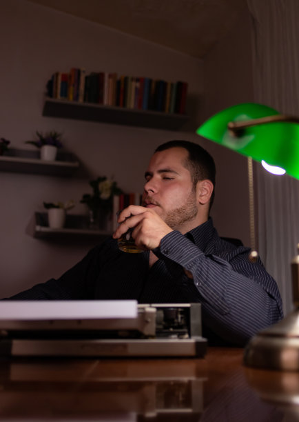 年轻的作家坐在他家里的房间里，用他的旧打字机写故事，思考故事应该写在哪里，然后检查他的文本，写。图片下载