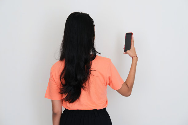 年轻亚洲女性的背影寻找手机，她持有图片下载