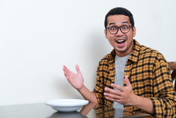 亚洲男子坐在空餐盘前，神情激动图片下载