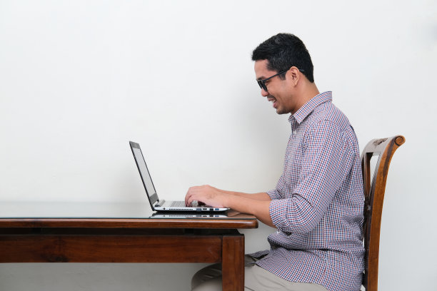 侧面的亚洲男人在他的笔记本电脑上打字，带着快乐的表情图片下载