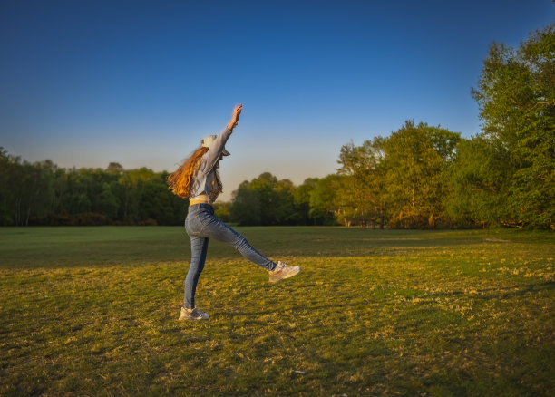 一个留着红色长发的少女在日落时分在公园里翻跟斗图片下载