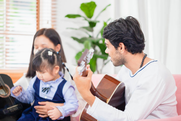 一家人在客厅的沙发上度过时光，快乐的父母和女儿在沙发上弹吉他，父亲和孩子弹吉他图片下载