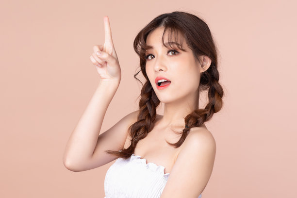 快乐开朗的年轻亚洲女性与两个辫子自然美容化妆，时尚模特，健康健康，美丽的女孩皮肤护理和面部治疗。孤立在米黄色粉红色的背景。图片下载