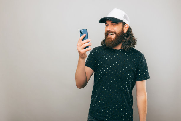 一名快乐的大胡子男子站在一堵灰色的墙边，正在和一个微笑的人发短信图片下载