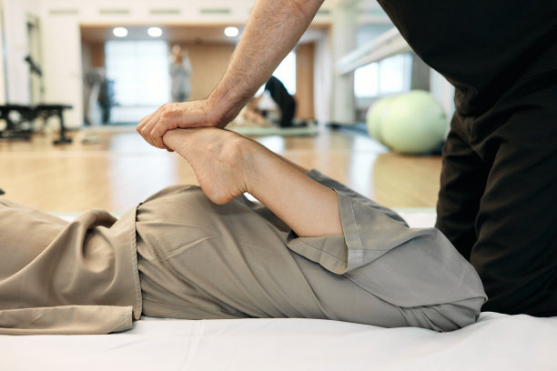 按摩师用日本手法Yumeiho按压女性患者弯曲的双腿，同时进行治疗按摩，侧视、特写。Yumeiho图片下载
