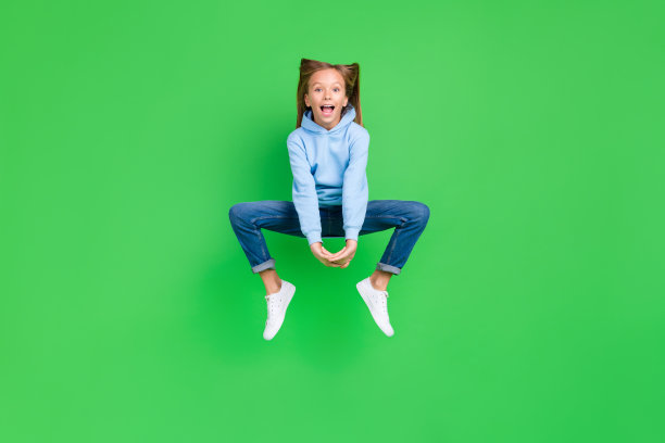 活泼的小女孩顽皮的跳床愚弄穿着时髦的蓝色运动衫孤立在绿色背景的全尺寸照片图片下载