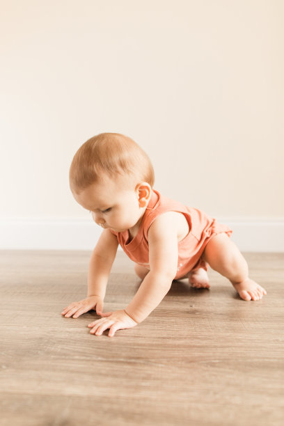 8个月大的大流行男婴，有12个脚趾，穿着写着“妈妈认为我是一个有趣的人”的鲑鱼色紧身泳衣，在木地板上玩的时候画上了蘑菇真菌图片下载