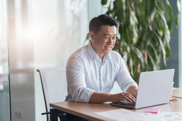 微笑的亚洲商人在现代化的办公室里用笔记本电脑工作图片下载