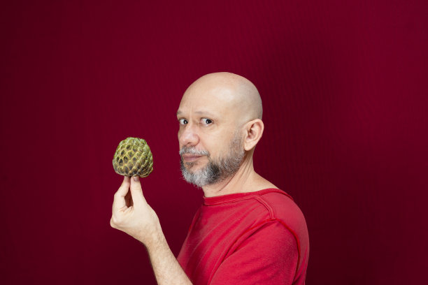 年轻英俊的男子，光头，红衬衫，手持松果站在红色的背景。图片下载