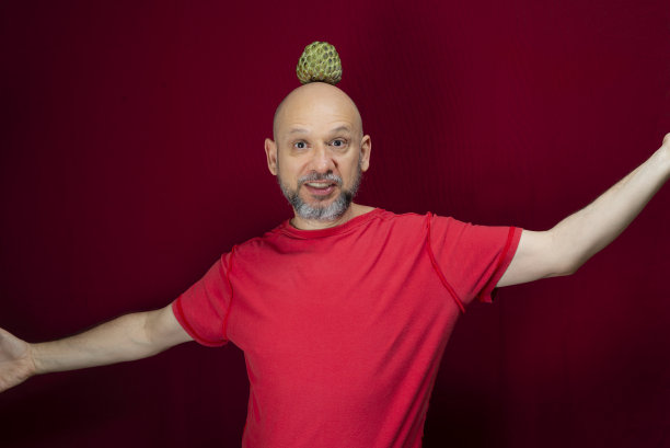 年轻英俊的男子与胡子，光头和红衬衫站与松果平衡的头在红色的背景。图片下载