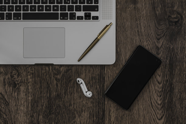 笔记本电脑，放在木桌上的笔记本电脑，配有智能手机，无线蓝牙耳机和一支金笔图片下载