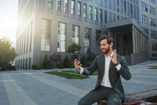 快乐的商人在休息时与朋友视频通话，坐在办公大楼的背景上图片下载