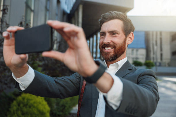 快乐的商人在休息时与朋友视频通话，坐在办公大楼的背景上图片下载