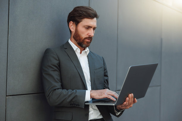 专注的商人在办公大楼外用笔记本电脑工作图片下载