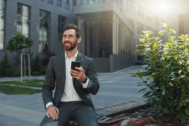 有吸引力的商人拿着电话坐在办公大楼附近休息图片下载
