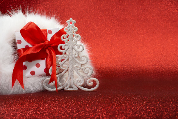 白色礼品盒与红点在圣诞老人的帽子和圣诞树在红色闪闪发光的背景。新年。本空间图片下载
