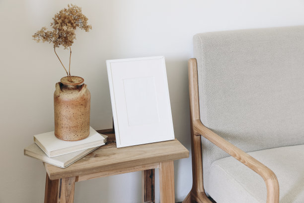 空的垂直画框模型。陶瓷花瓶与干绣球花在一堆旧书。本世纪中叶亚麻沙发。白墙的背景。北欧室内，客厅设计。图片下载