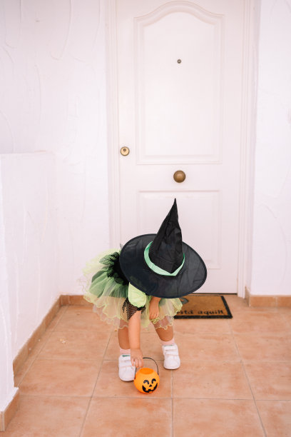 穿着女巫服装的小女孩在白色的门口玩不给糖就捣蛋的游戏图片下载